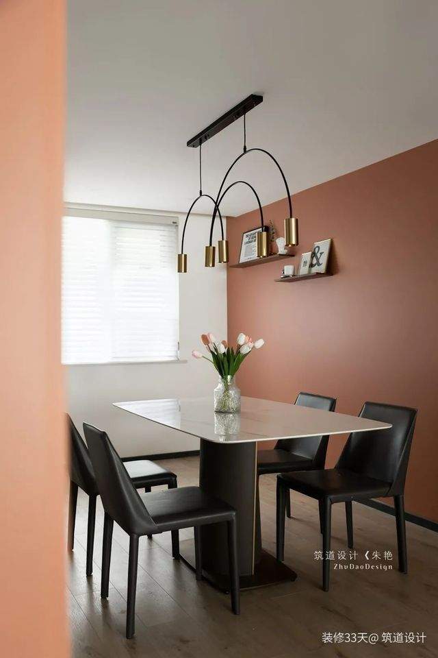 餐廳延續橙色乳膠漆，巖板餐桌搭配皮質餐椅，結合一盞金屬弧線吊燈提升就餐格調